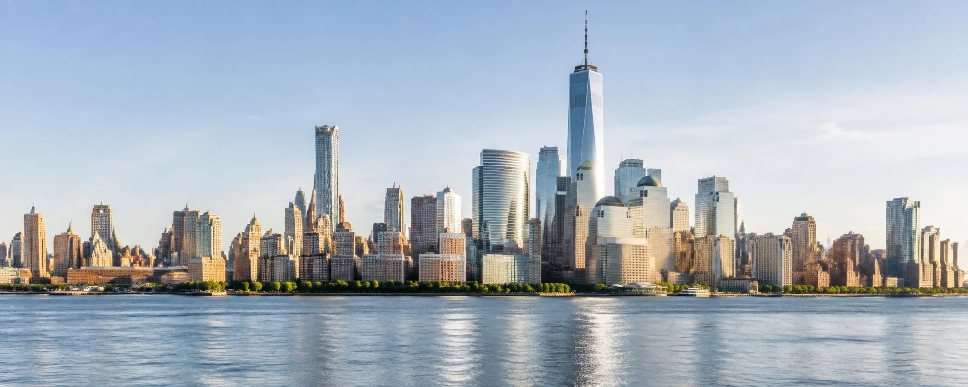 Sunlit skyscrapers in Manhattan's financial district, including One World Trade Center, across the East River